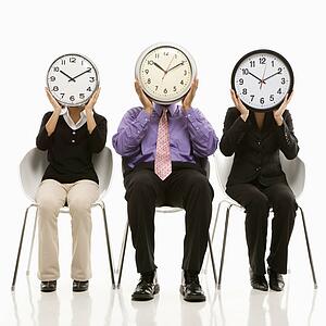 Business people in chairs holding clocks over their faces