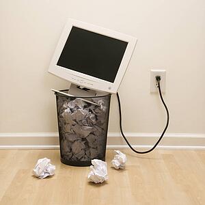 Computer monitor in trash can surrounded by crumpled up paper