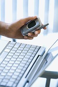 Close up of young woman's hand holding cellphone with laptop in background