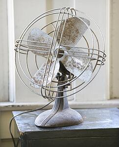 Retro style metal fan sitting on tabletop by window.