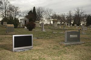 Flat panel television set in cemetery next to headstone
