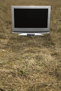 Flat panel television set in grassy field.