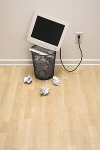 Computer monitor in trash can surrounded by crumpled up paper