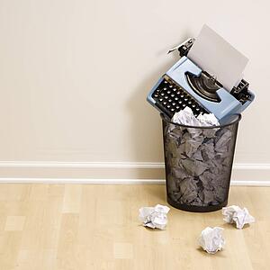 Old fashioned typewriter in trash can surrounded by crumpled up paper.