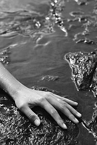 Close up of young adult female hand in water on rocks