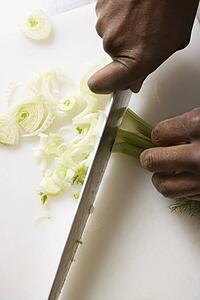 Male hands using large kitchen knife to chop fennel