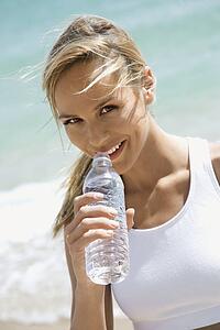 Caucasian young adult woman drinking water on beach.