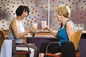Mature Asian and Caucasian adult females sitting at table in health club cafeteria.