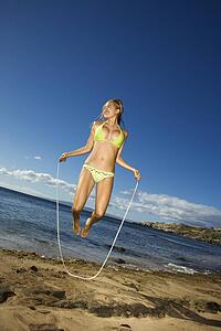 Young adult Asian Filipino female in bikini jumping rope on beach 