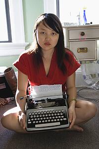 Pretty Asian young woman sitting on floor in red robe holding typewriter.