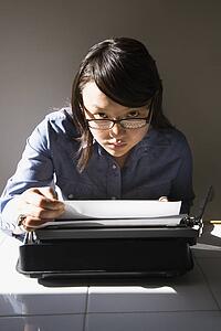 Woman with typewriter making eye contact over glasses