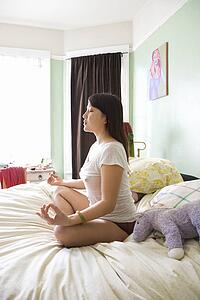 Woman sitting on bed in underwear and t-shirt meditating in lotus pose