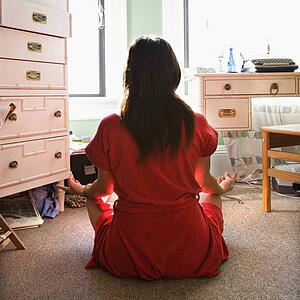 Woman in red robe sitting on floor meditating in lotus pose