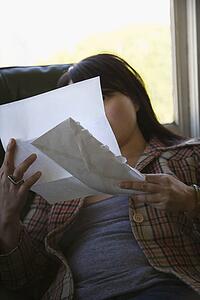 Young Asian woman sitting in green chair reading letter.