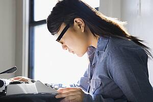 Pretty young woman sitting in chair typing on typewriter in kitchen