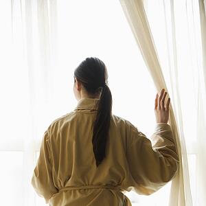 Taiwanese mid adult woman in bathrobe looking out window.