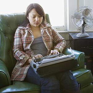 Pretty young woman sitting in green chair typing on typewriter