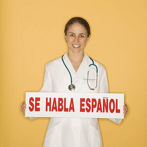 Portrait of doctor holding up se habla espanol sign against yellow background