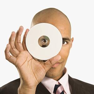 Man holding compact disc over face and peeking through hole