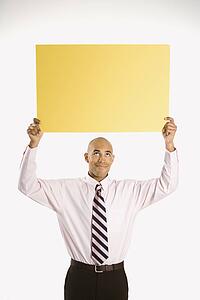 Man holding blank yellow sign overhead standing against white background