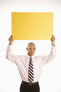  man holding blank yellow sign overhead standing against white background.