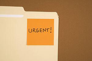 Folder with an orange sticky note attached reading urgent on brown background