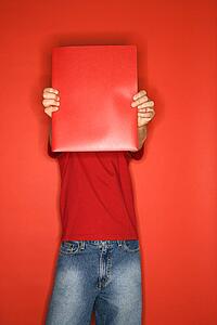 Portrait of boy covering his face with red folder standing against red background
