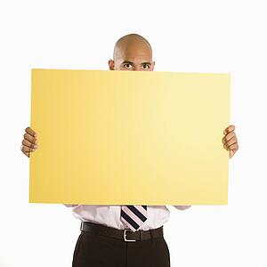 Man holding and peeking over blank yellow sign