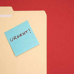 Folder with a blue sticky note attached reading urgent on a red background