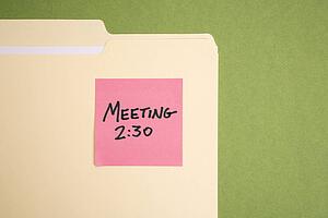Folder with pink sticky note reminder for a meeting on a green background