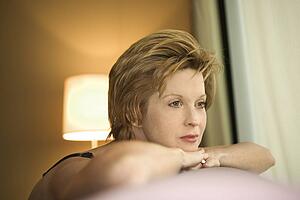 Portrait of pretty woman draped over sofa by window looking out.