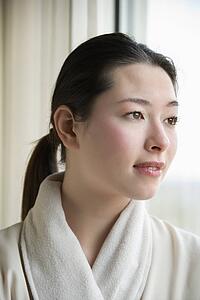 Taiwanese mid adult woman in bathrobe looking out window.