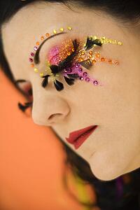 Woman with unique makeup with eyes closed against orange background