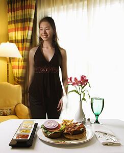 Room service cheeseburger meal with flowers and Taiwanese mid adult woman in background.