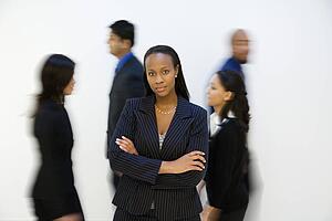 African-American businesswoman standing with arms crossed while others walk by.