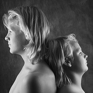 Adolescent and teen brothers standing back to back.