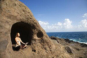 Young Asian woman mediatating in cave with coastline 