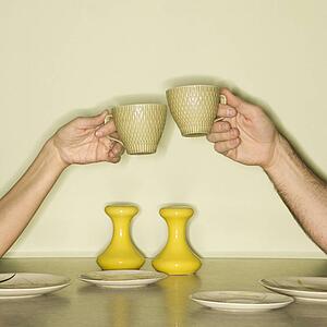 Couple toasting with coffee cups across retro kitchen table setting
