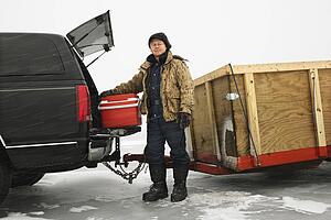Man unloading cooler from truck with trailer on frozen lake going ice fishing in Green Lake, Minnesota