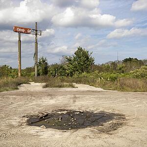Old sign in rural setting with mud puddle in foreground.
