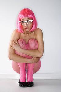 Portrait of attractive Caucasian young adult woman wearing pink wig and pink fishnet stockings, kneeling and hugging herself with anxious expression.