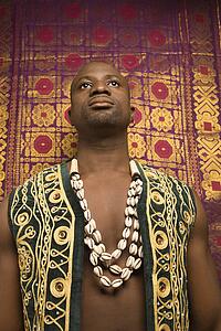 Low angle portrait of mid-adult man wearing embroidered African vest and beads