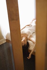 Pretty young woman lying on bed with head hanging over wearing nightgown.