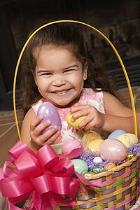 Hispanic girl holding egg from Easter basket looking at viewer smiling.