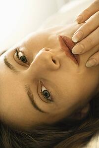 Close up portrait of Caucasian mid-adult woman looking at viewer touching fingers to lips.
