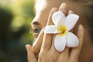 Woman holding plumeria flower over eye