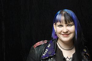 Portrait of smiling Caucasian woman with blue hair and black leather jacket against black background.
