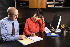 Businessman and businesswoman in office going over appointment calendar.