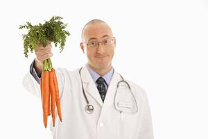 Caucasian mid adult male physician holding bunch of carrots.