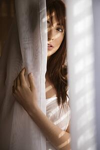 Woman standing in sunlit curtains